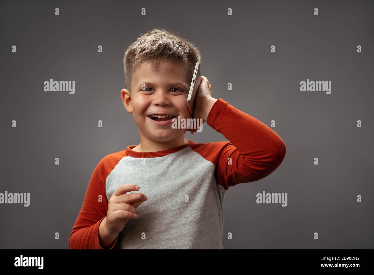 Un petit garçon caucasien avec une coupe de cheveux courte. Communication joyeuse au téléphone. Sur fond gris Banque D'Images