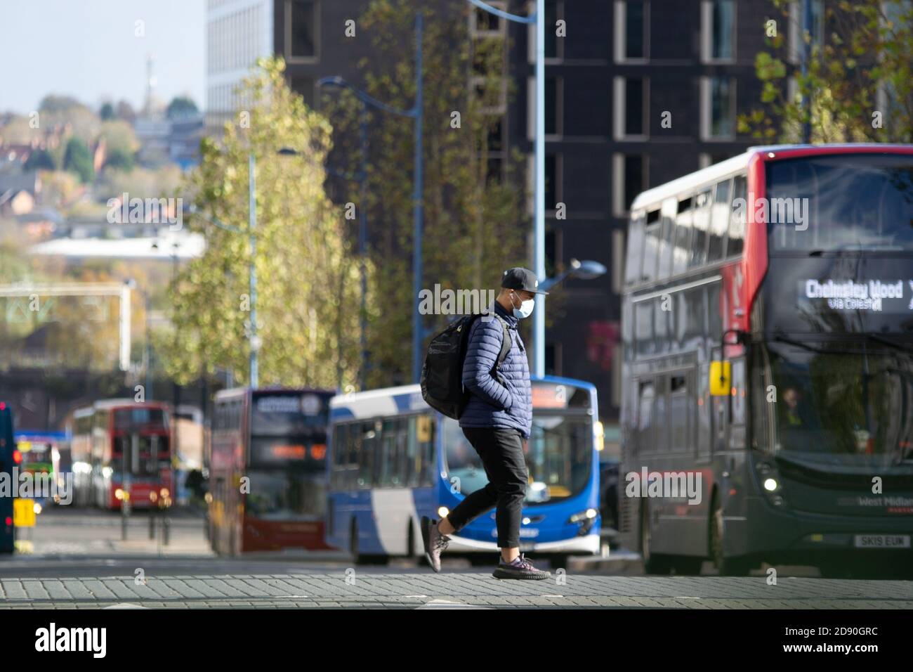 Un homme portant un masque de visage marche de l'autre côté de la rue à Birmingham Avec l'entrée en vigueur jeudi de restrictions plus sévères en matière de verrouillage Banque D'Images