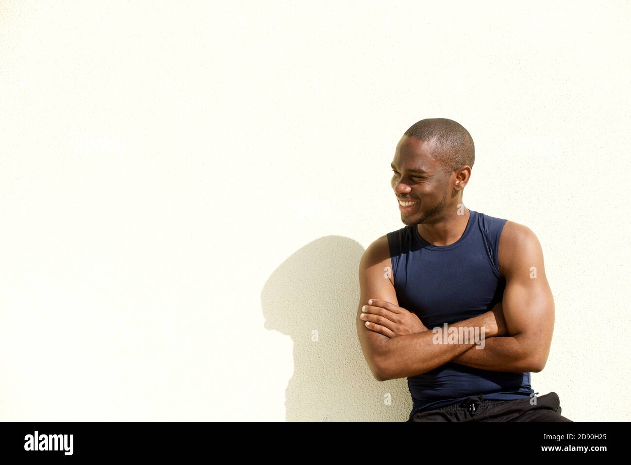 Portrait d'un jeune homme africain sportif souriant contre un mur blanc Banque D'Images