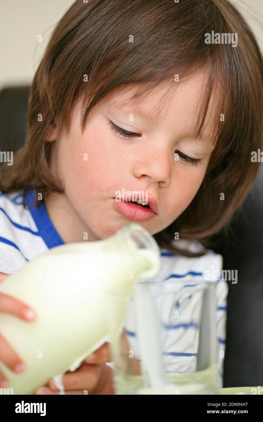Un petit garçon de l'école verse un verre de lait frais à la table du petit déjeuner, Powys, pays de galles. ©PRWPhotography Banque D'Images