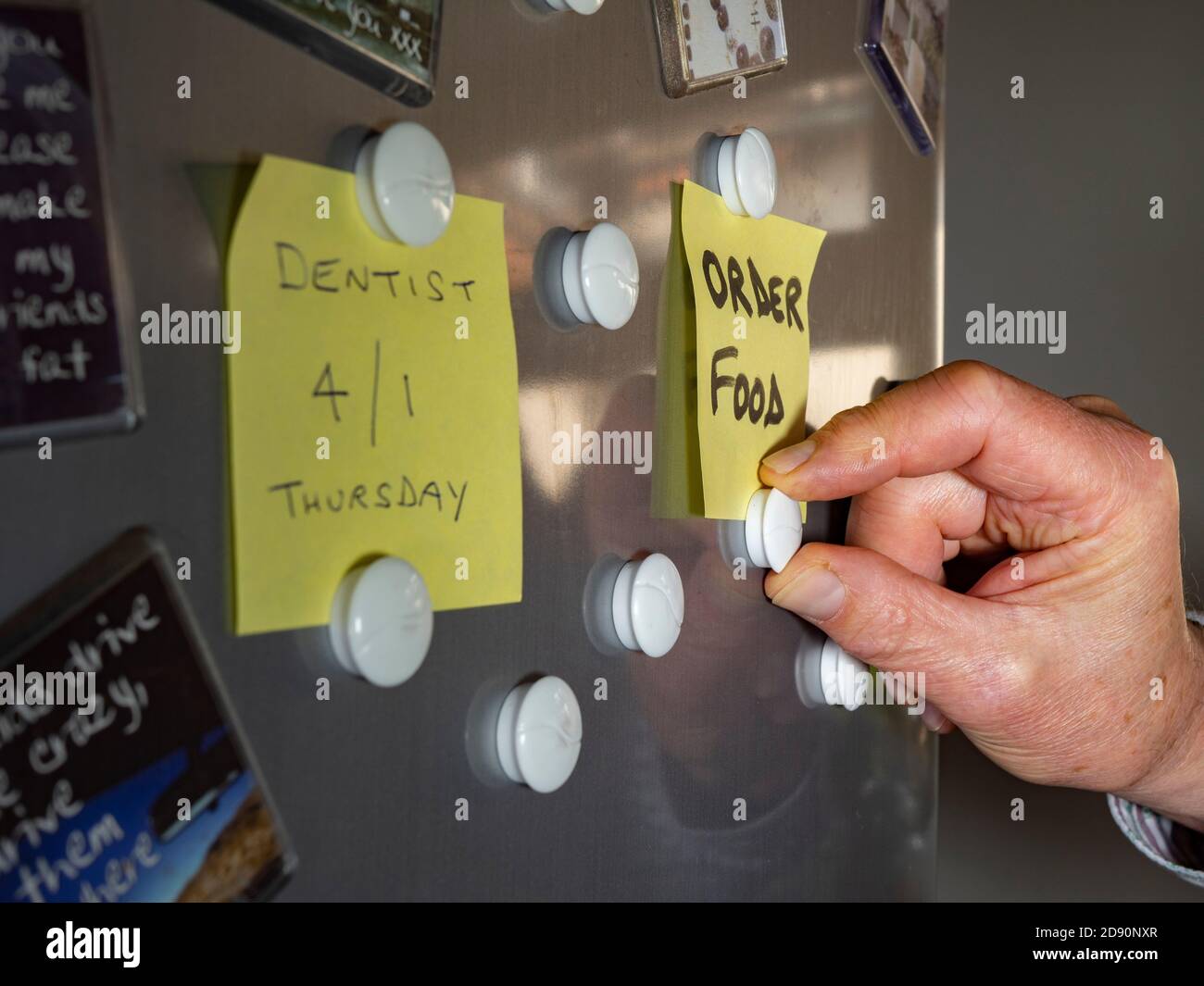 Gros plan de la main d'un homme en collant une note pour commander des aliments sur une porte de réfrigérateur, à l'aide d'aimants. Banque D'Images