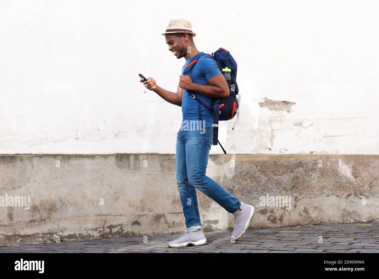 Portrait du côté du corps complet d'un touriste afro-américain heureux marche avec sac et téléphone portable Banque D'Images