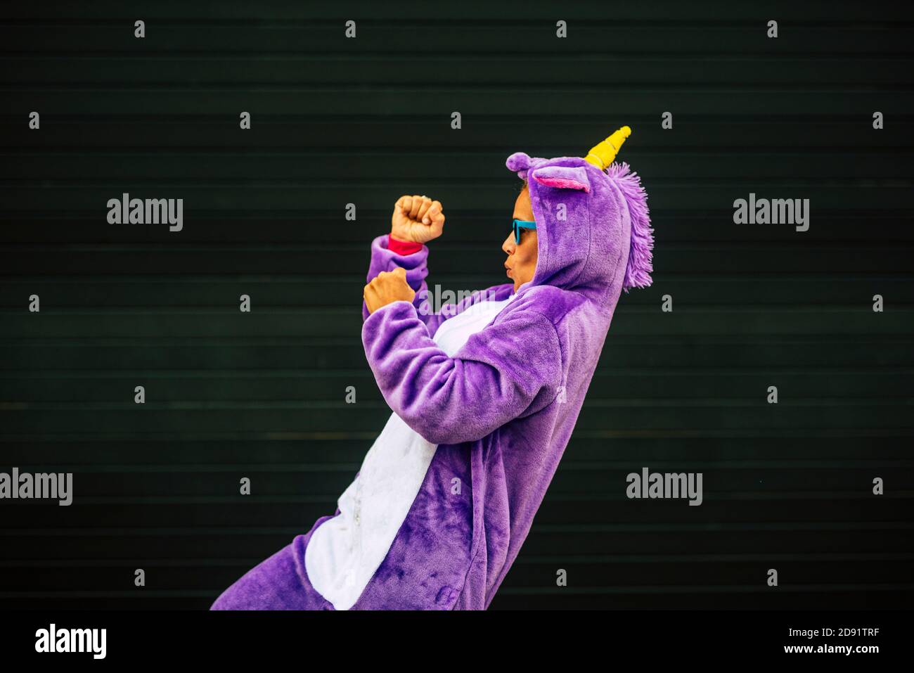 Fou masque de licorne danse avec des gens drôles - joyeux et joyeux femme dansant avec une robe de carnaval avec un mur noir en arrière-plan - le plaisir et le bonheur concep Banque D'Images