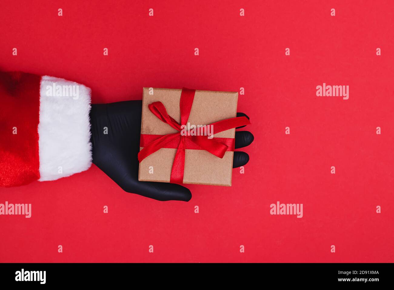 Un gant de protection tient une boîte cadeau rouge avec un ruban Banque D'Images