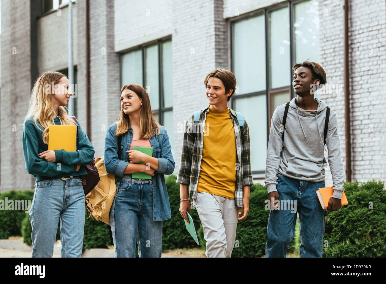 Adolescents multiethniques regardant un ami avec un ordinateur portable tout en marchant rue urbaine Banque D'Images