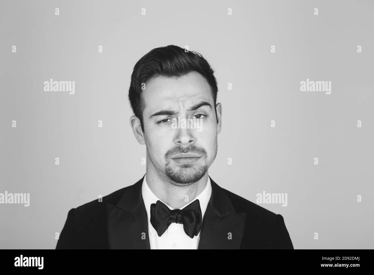 Studio portrait d'un jeune homme caucasien dans un tuxedo, fait un visage, regardant la caméra, sur fond de studio simple Banque D'Images