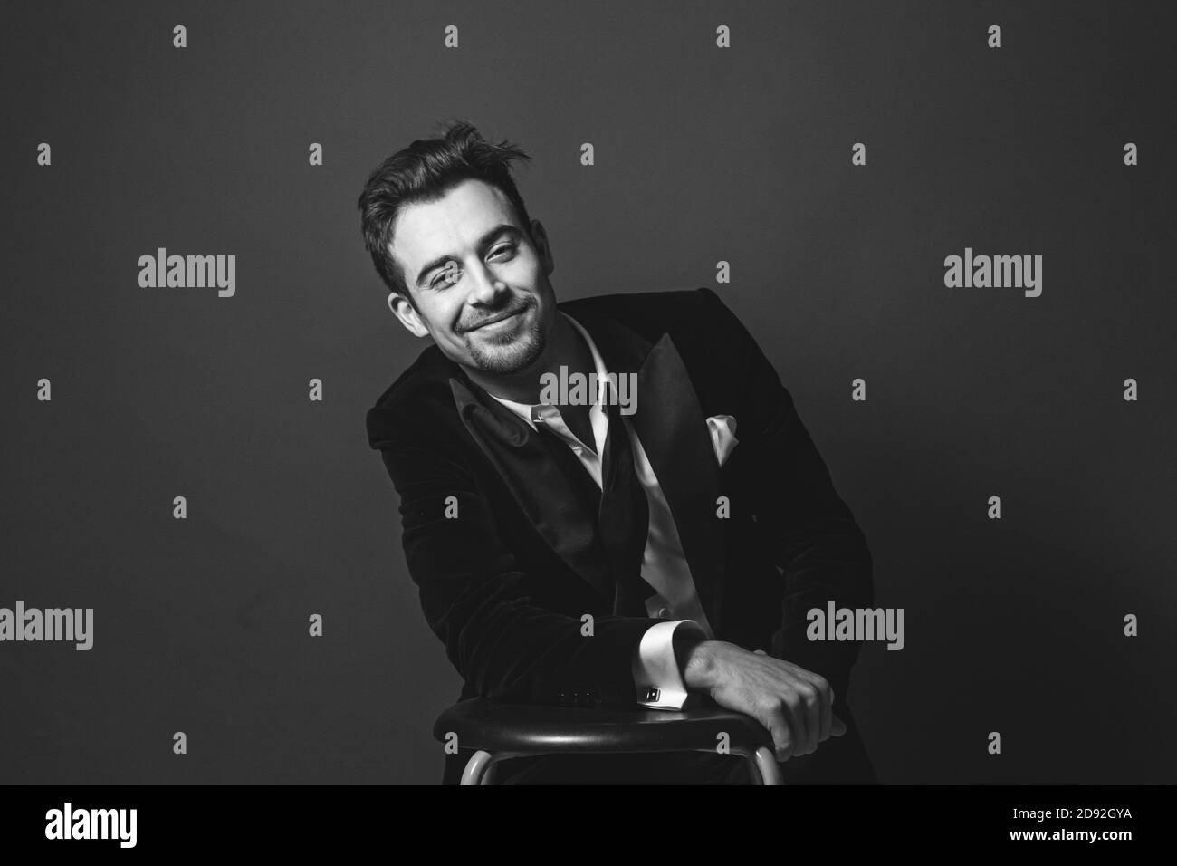 Studio portrait d'un jeune homme caucasien dans un tuxedo, souriant, regardant la caméra, sur fond de studio simple Banque D'Images