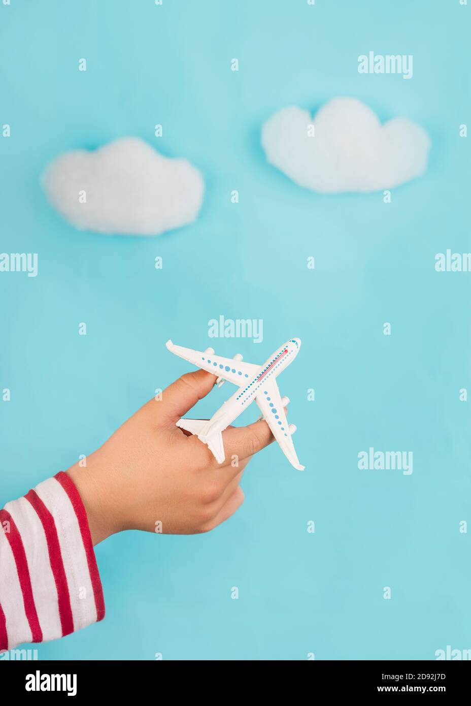 mains d'enfant tenant un avion jouet sur des nuages sur fond bleu. Concept de voyage Banque D'Images