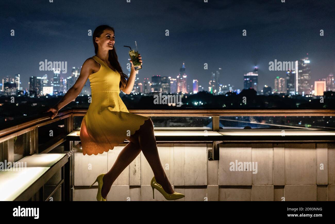 Femme prenant un verre sur la terrasse du toit donnant sur la ville Banque D'Images
