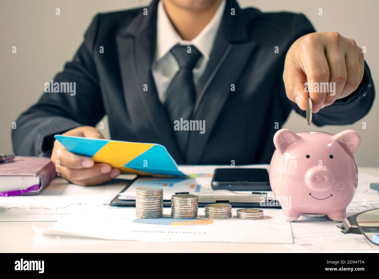 Un homme d'affaires détient une pièce de monnaie sur la banque de porc pour économiser de l'argent pour des idées d'investissement, de l'épargne et des investissements durables. Banque D'Images