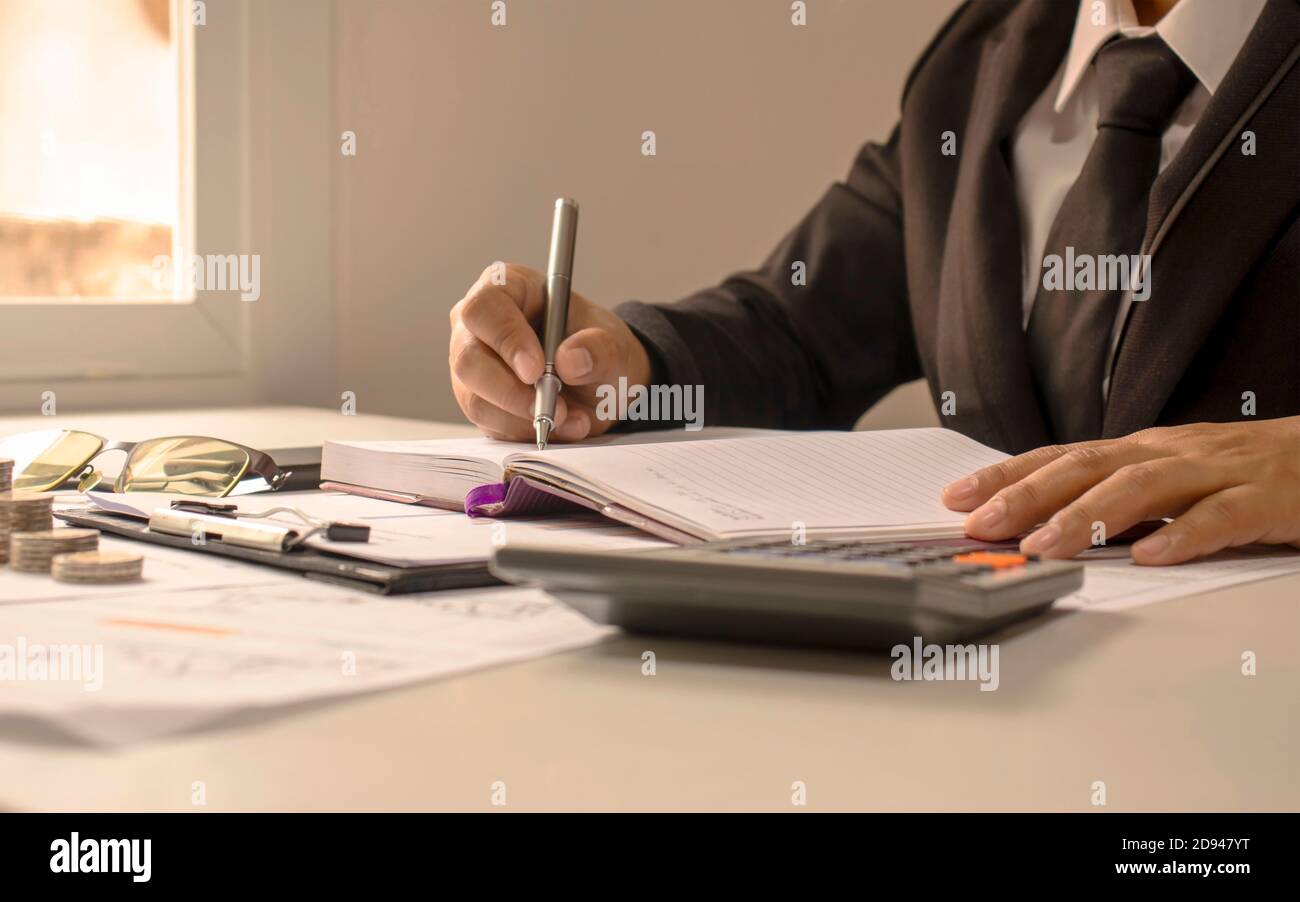 Gros plan d'un homme d'affaires prenant des notes dans un livre pour examiner les rapports comptables, les idées de vérification financière, et enregistrer les revenus et les dépenses. Banque D'Images