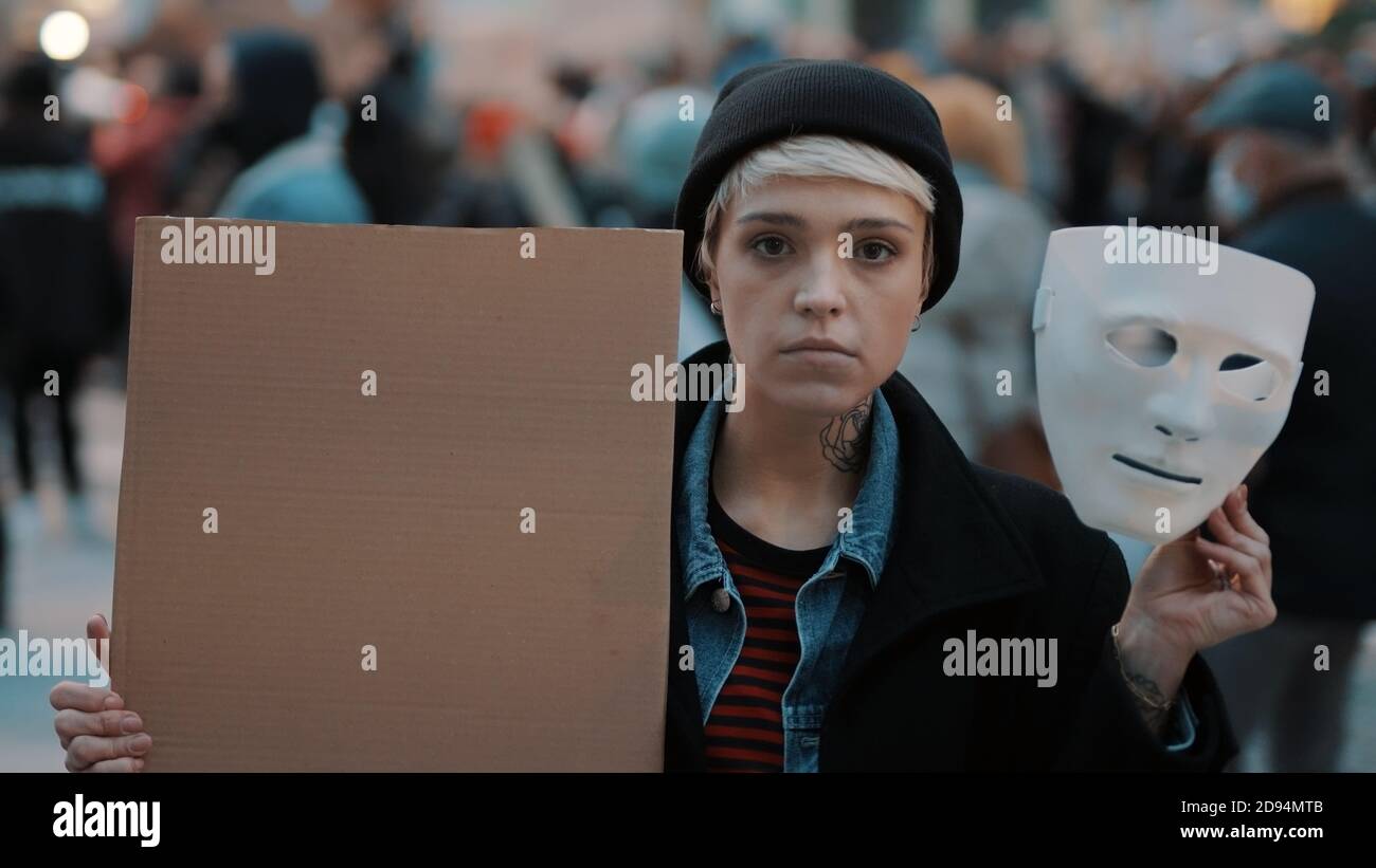 Jeune femme qui retire le masque de théâtre tout en tenant du carton noir dans la foule. Protestation contre la discrimination. Photo de haute qualité Banque D'Images