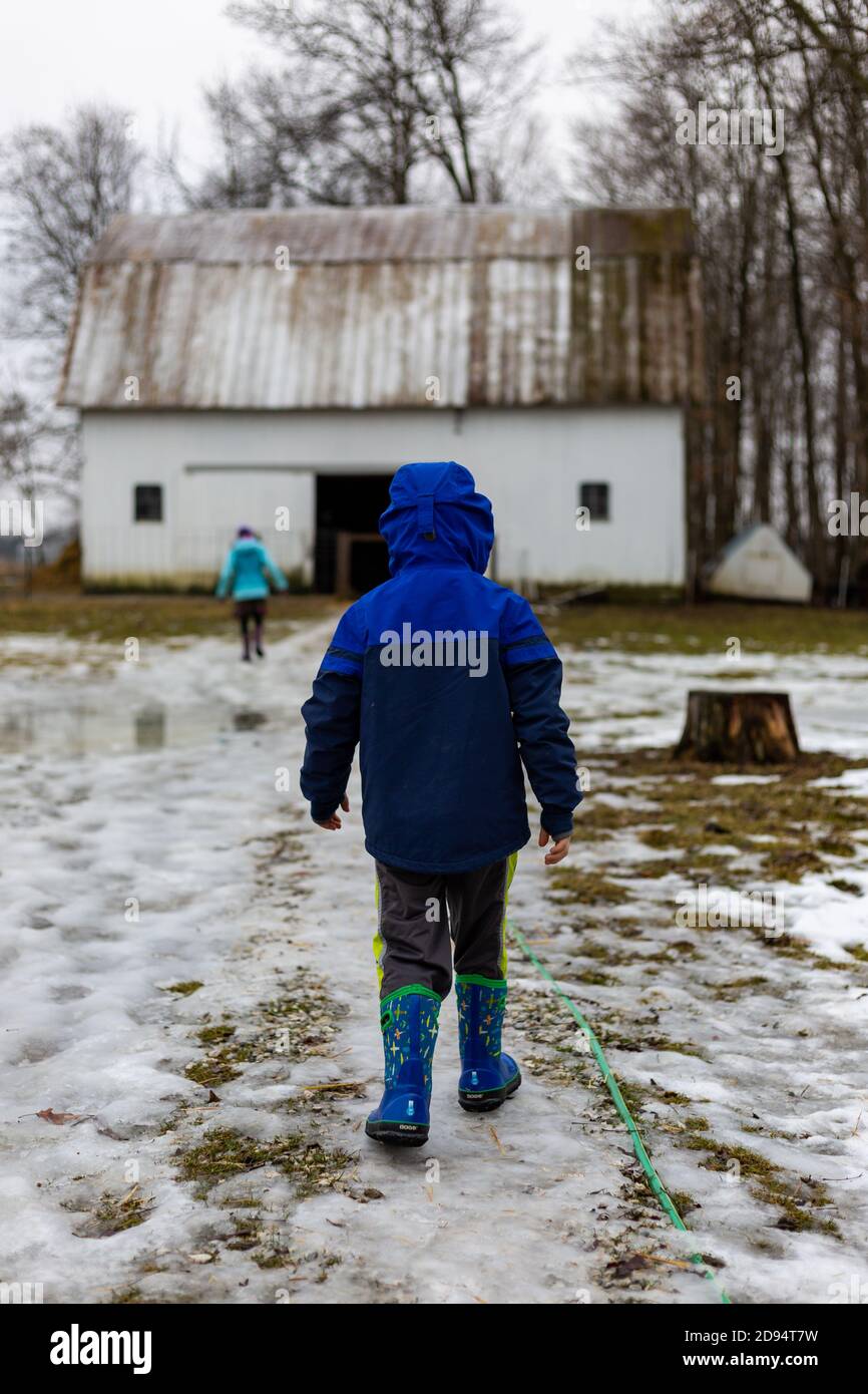 Un garçon de manteau bleu suit sa sœur jusqu'à la grange de la ferme du comté de DeKalb, près de Spencerville, Indiana, États-Unis. Banque D'Images