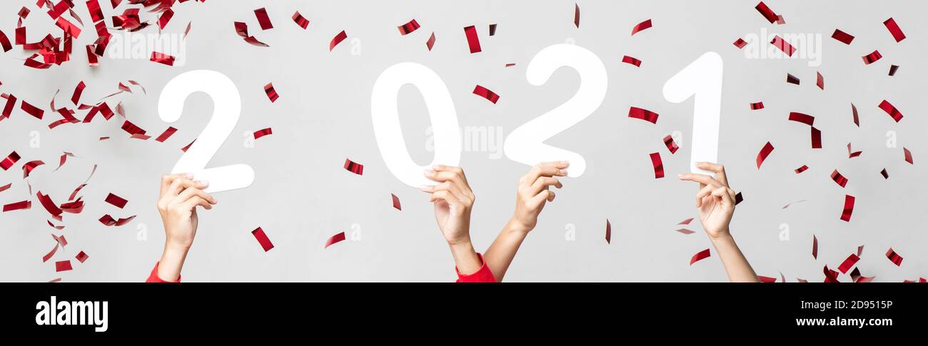 Mains de 2021 chiffres avec confetti rouges sur gris clair arrière-plan de la bannière pour le concept de la nouvelle année heureuse Banque D'Images