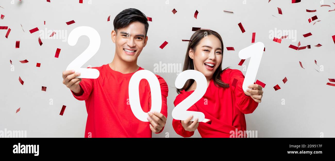 Sourire heureux asiatique couple en rouge décontracté tenue 2021 chiffres pour le nouveau concept de l'année sur fond de bannière gris clair avec confettis Banque D'Images