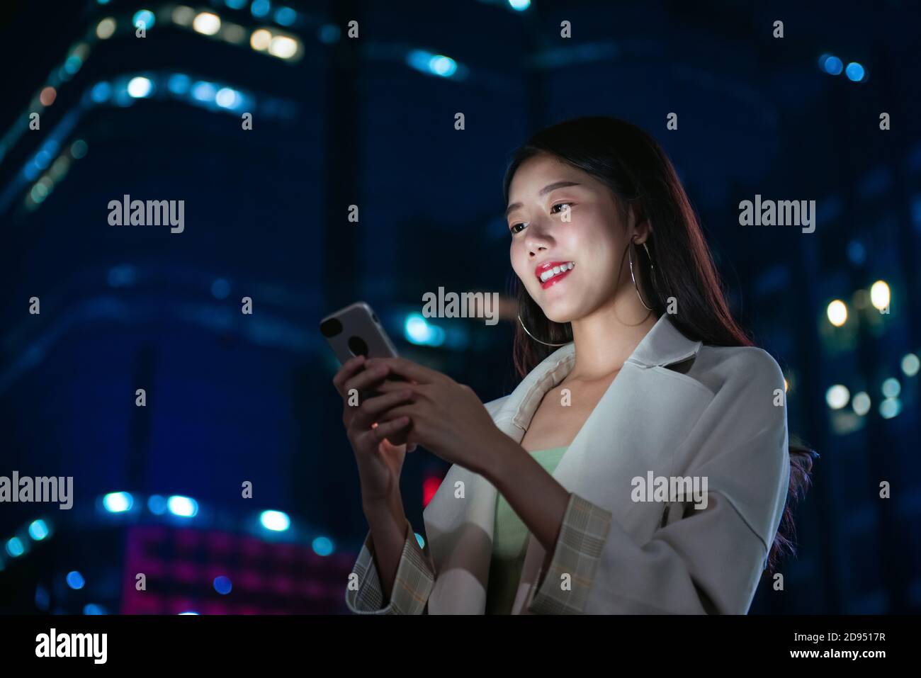 Portrait d'une belle jeune femme asiatique utilisant un smartphone dans le ville la nuit Banque D'Images