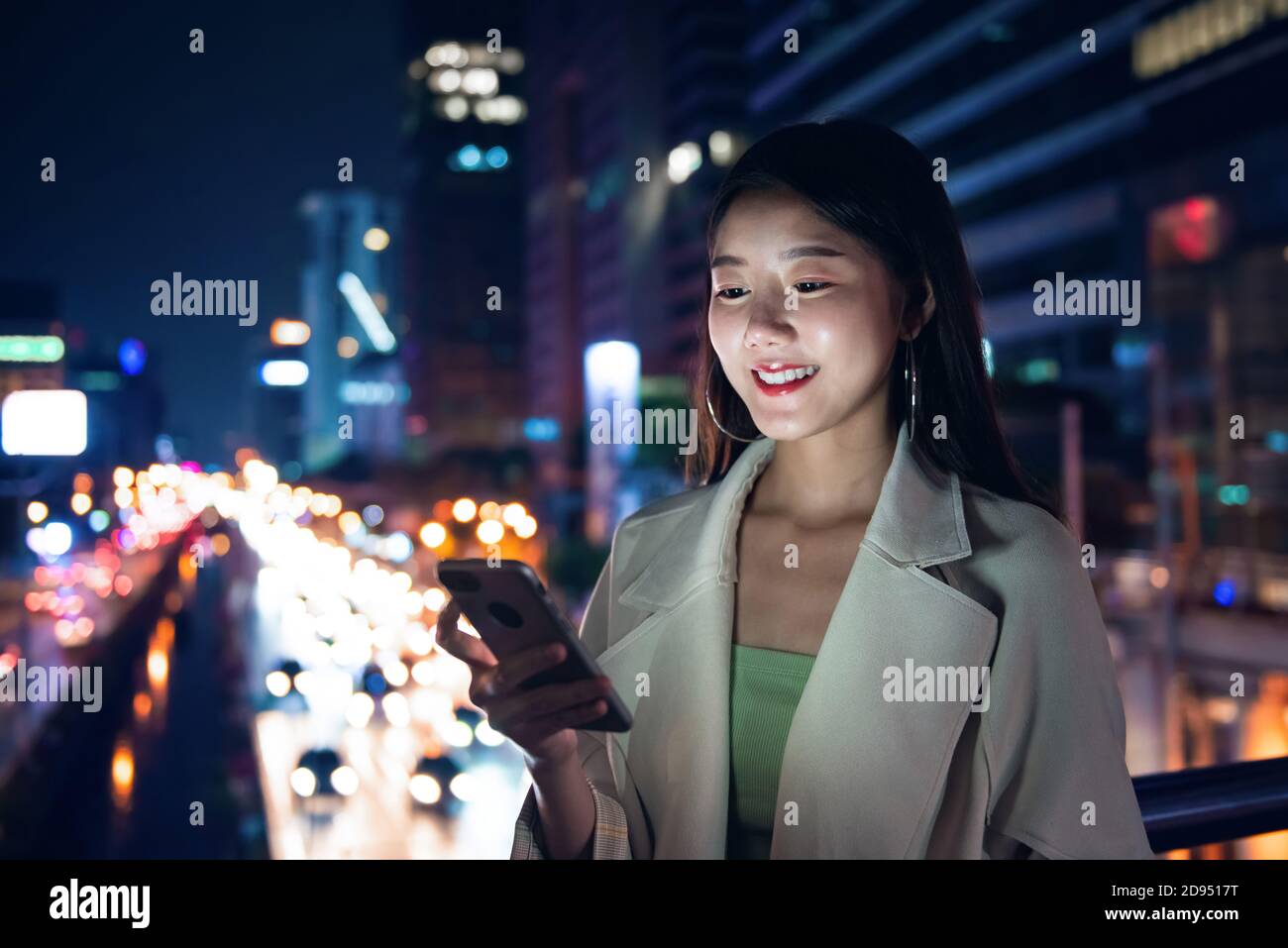 Belle femme asiatique utilisant le téléphone mobile la nuit sur flou vue sur la ville et la rue avec lumière bokeh Banque D'Images