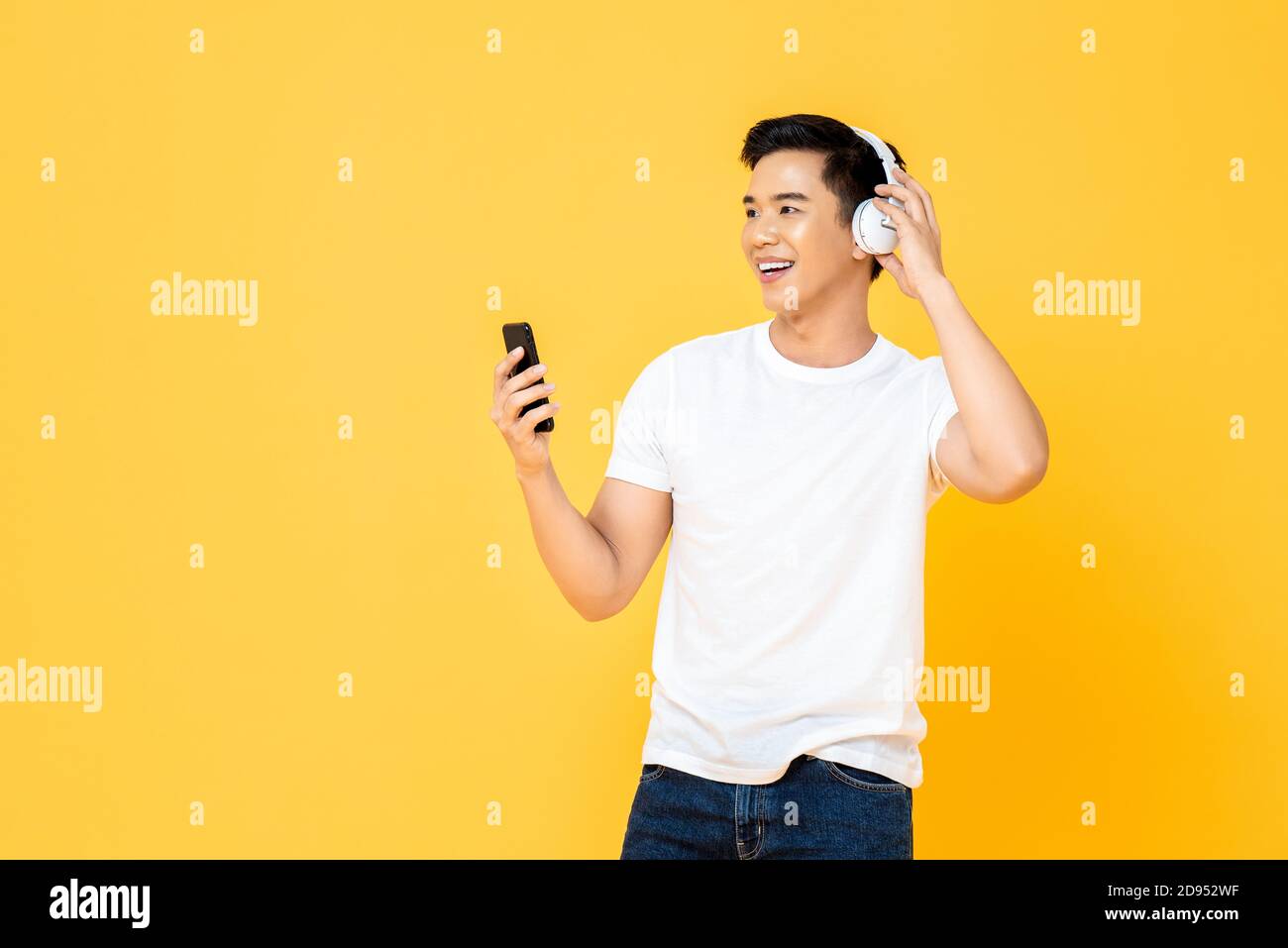 Jeune homme asiatique élégant portant un casque pour écouter de la musique depuis un smartphone sur fond jaune Banque D'Images