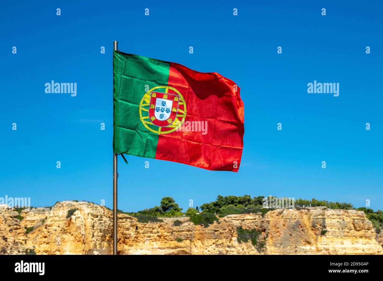 Accent sélectif sur l'agissement du drapeau du portugal devant la formation typique de roche jaune de l'algarve et du ciel bleu. Drapeau national du portugal avec espace. Banque D'Images