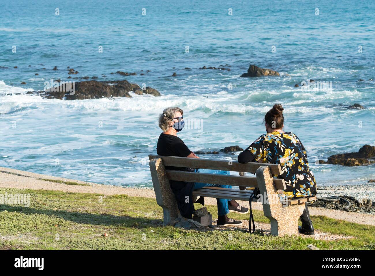 deux femmes discutent sur un banc surplombant l'océan ou de la mer pendant une pandémie portant des masques faciaux et de maintien un virus corona de concept de distance de sécurité Banque D'Images