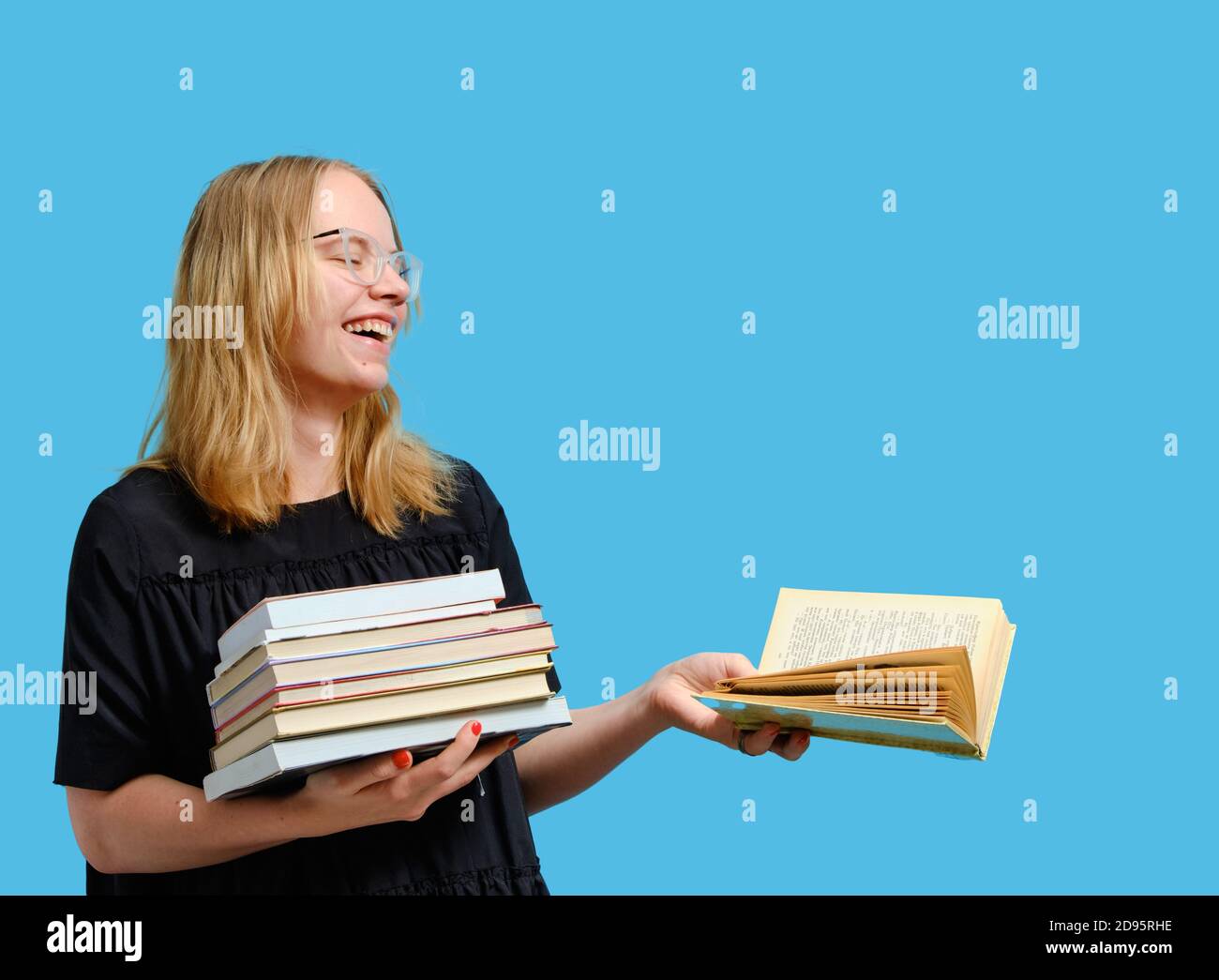 Studio portrait en demi-longueur d'un joyeux étudiant caucasien avec des livres en mains et lit un livre ouvert. Banque D'Images