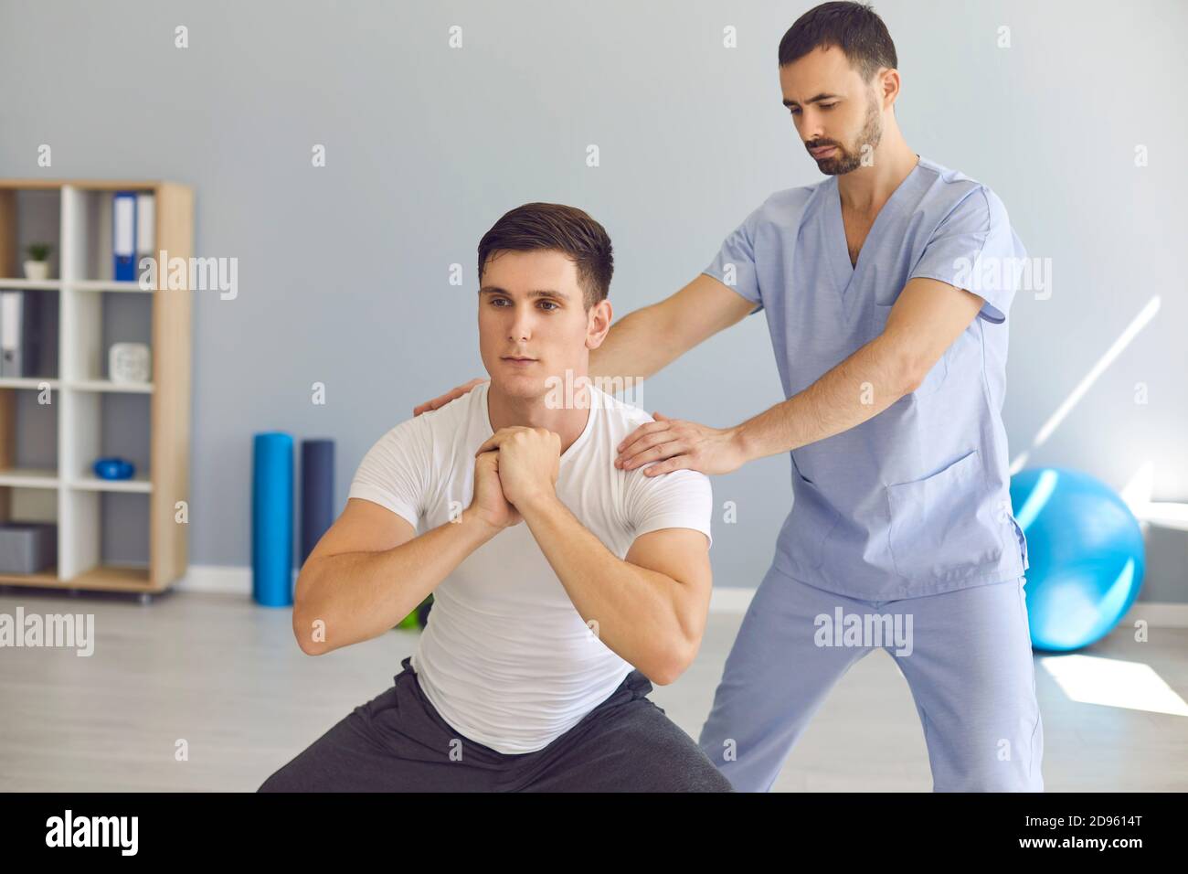 Physiothérapeute aidant les jeunes athlètes à faire des squats pendant la thérapie de réadaptation après blessures sportives Banque D'Images