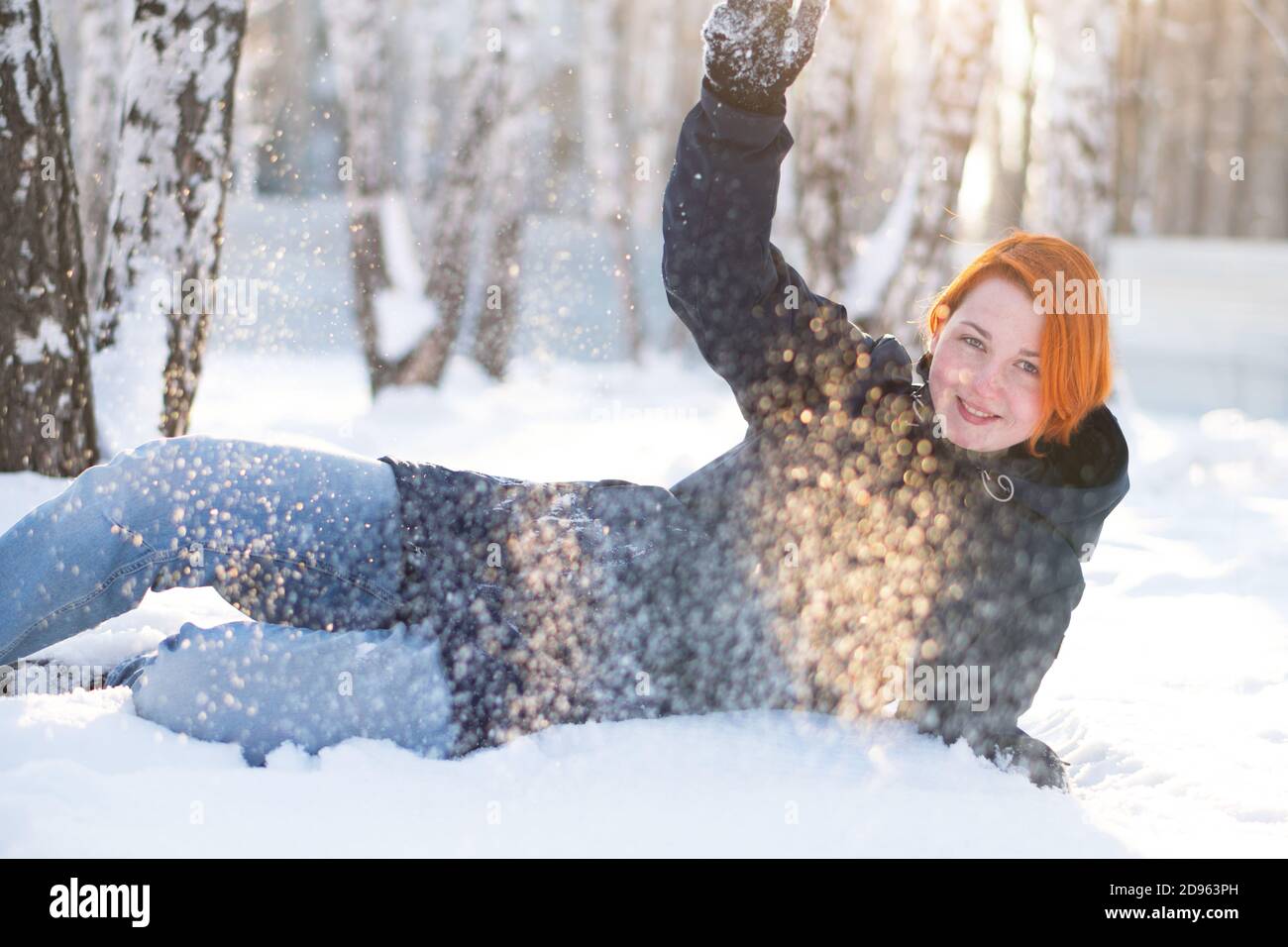 Fille veut jouer boules de neige tandis que se trouve dans la neige en forêt d'hiver. Femme entourée de flocons de neige. Banque D'Images