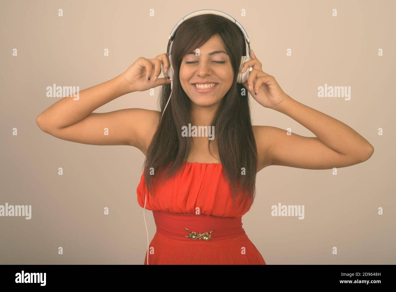 Studio shot of young woman smiling persan heureux tout en écoutant de la musique avec les yeux fermés à l'arrière-plan gris Banque D'Images