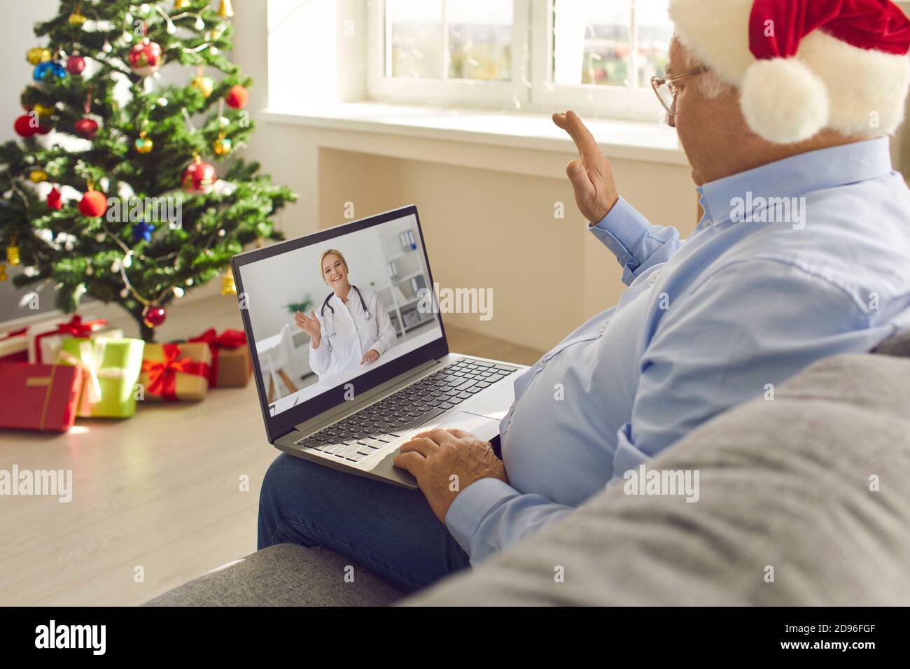 Homme senior assis sur un canapé à la maison et en agitant la main sur l'écran de l'ordinateur portable salutation médecin en ligne Banque D'Images