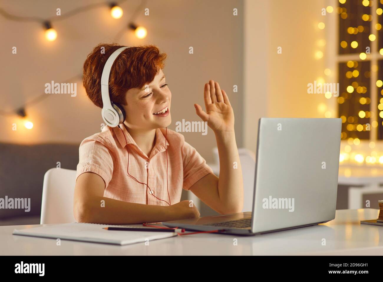Sourire rouge cheveux garçon dans le casque saluant enseignant ou quelqu'un pendant la leçon en ligne Banque D'Images