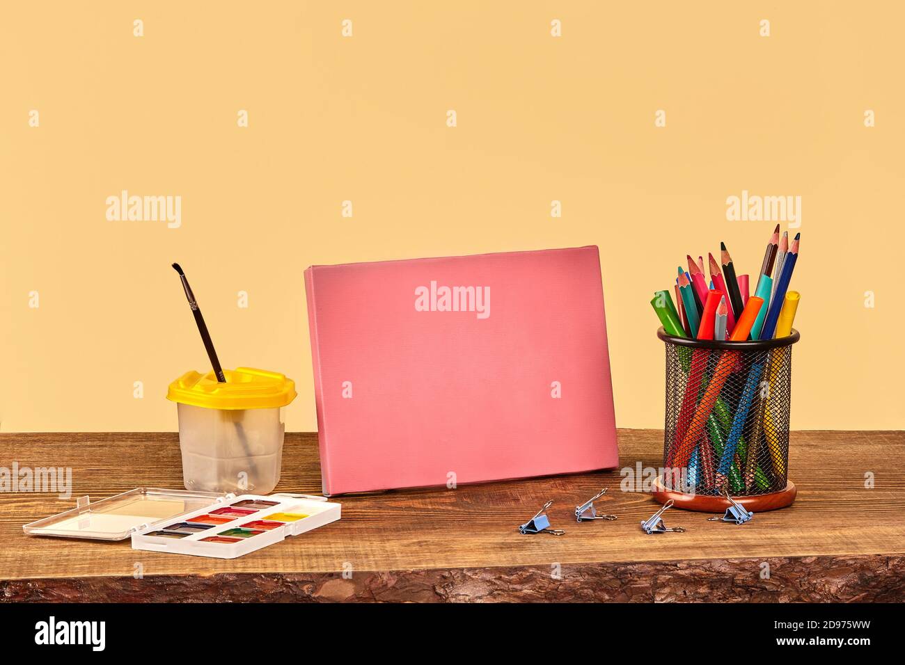 Toile rose, aquarelle, pinceau, pinces à reliures, stylos feutres et crayons colorés sur bureau en bois. Arrière-plan beige. Gros plan, espace de copie Banque D'Images