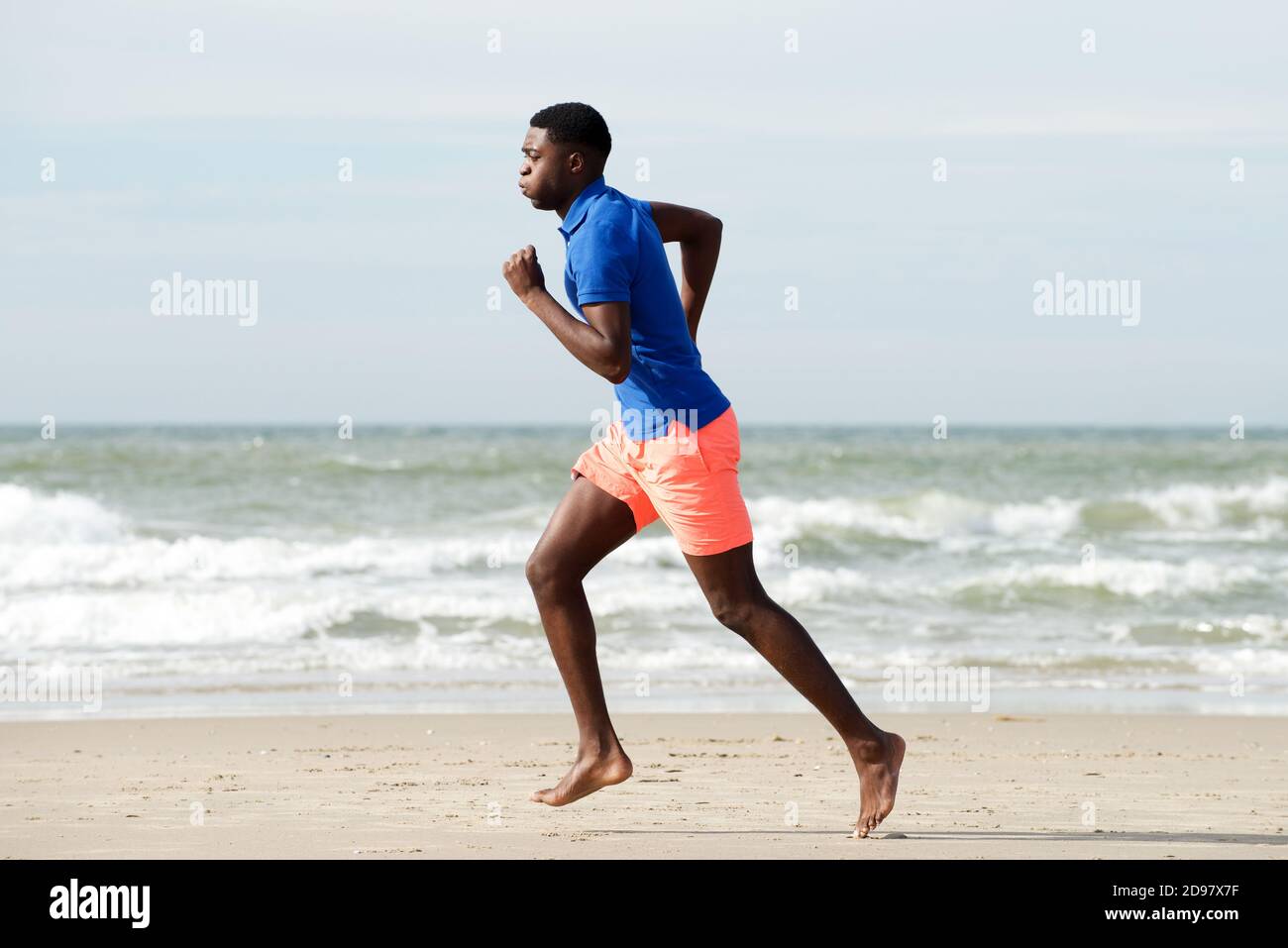 Homme afro-américain plein corps en bonne santé, course pieds nus à la plage Banque D'Images