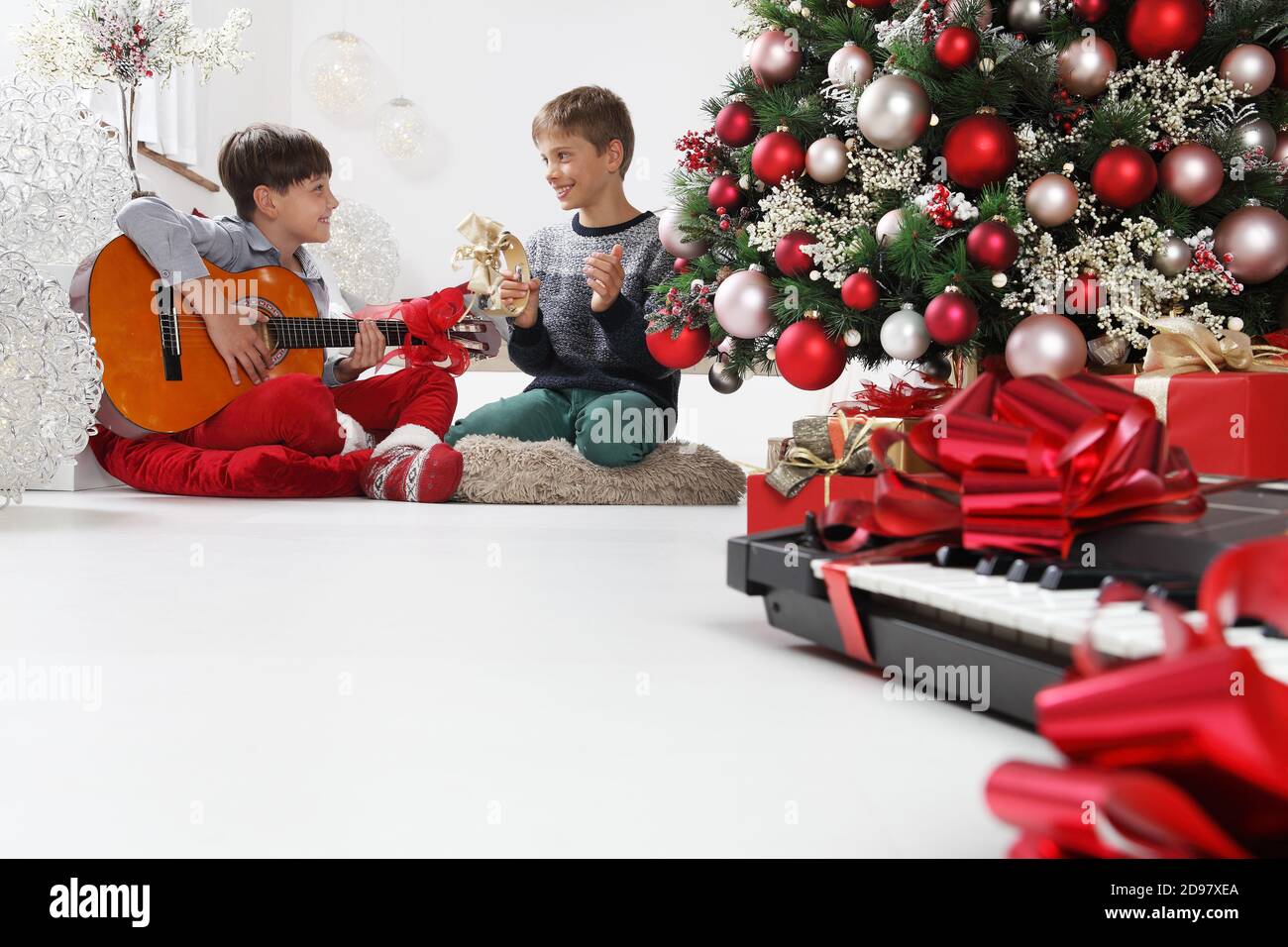 joyeux noël et joyeuses fêtes, les enfants jouent de la guitare et du  tambourin près de l'arbre de noël avec des paquets-cadeaux et des  instruments de musique emballés, à Photo Stock -