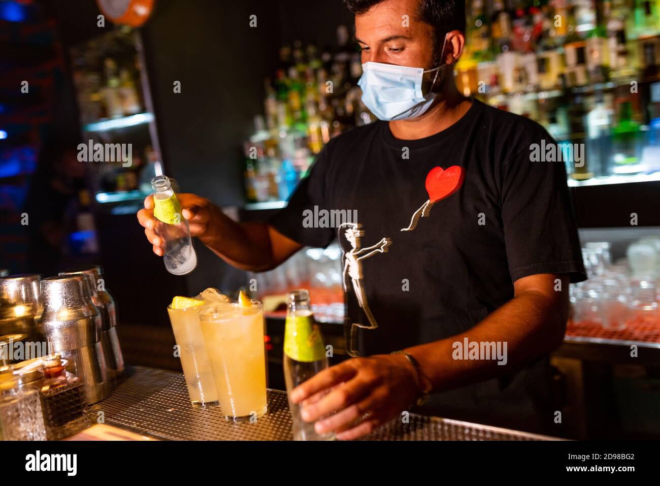 jeune barman avec masque visage verser cocktail à l'intérieur du bar. secteur de l'accueil a été gravement affecté par la crise du virus corona Banque D'Images