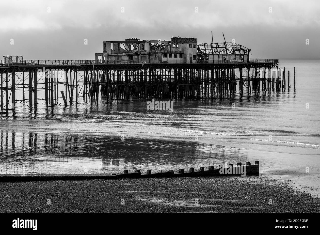 Vue monochrome du Gaunt et de l'épave tordue de Hastings Pier dans East Sussex, Angleterre, Royaume-Uni, photographiée sept mois après le feu dévastateur de 2010. La jetée victorienne, ouverte en 1872, a accueilli d'importants spectacles de rock et de pop dans les années 1960, dont Pink Floyd, Jimi Hendrix, les Rolling Stones et l'OMS. Un incendie a détruit le pavillon de la jetée Hastings de 2,000 places en 1972, la jetée a été fermée comme une structure dangereuse et l'incendie a détruit le 5 octobre 2010 ses bâtiments en bois restants. Les travaux de reconstruction ont été lancés en 2011 et la jetée a été rouverte en 2016. Banque D'Images