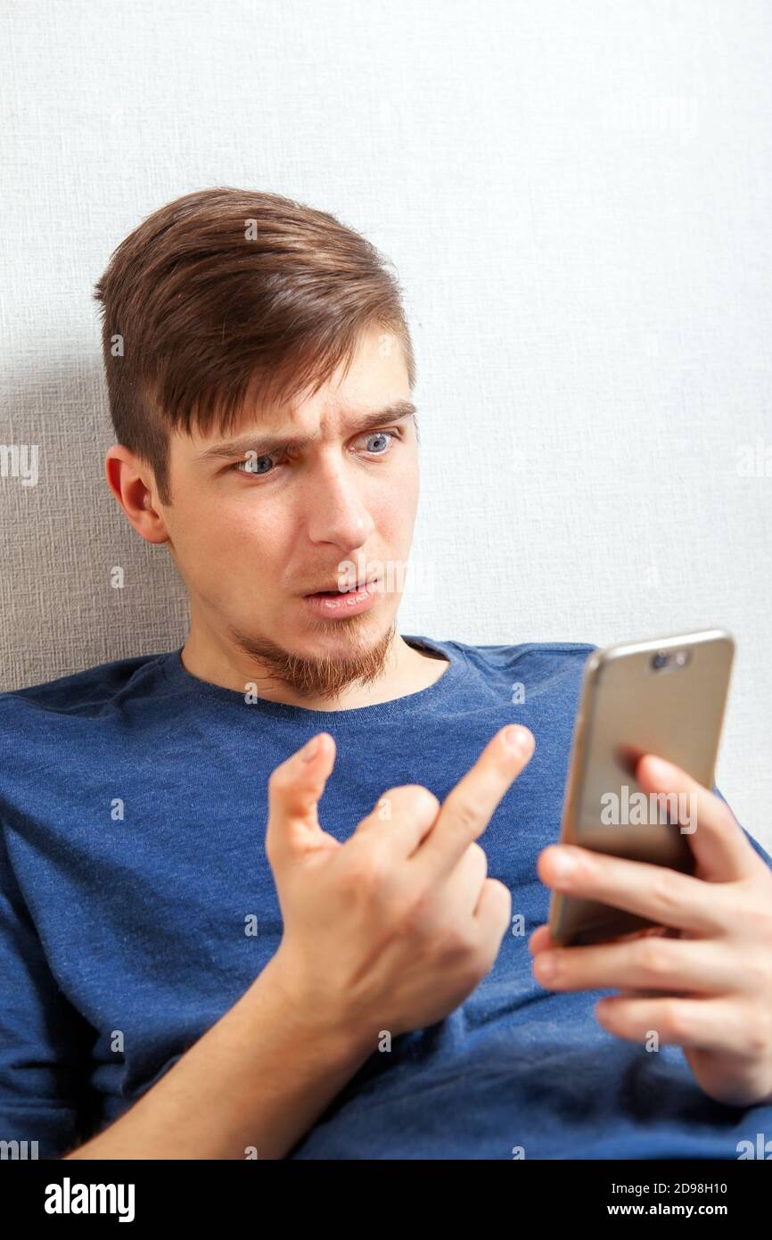 Jeune homme insatisfait montre le doigt du milieu au téléphone par Le mur dans la pièce Banque D'Images
