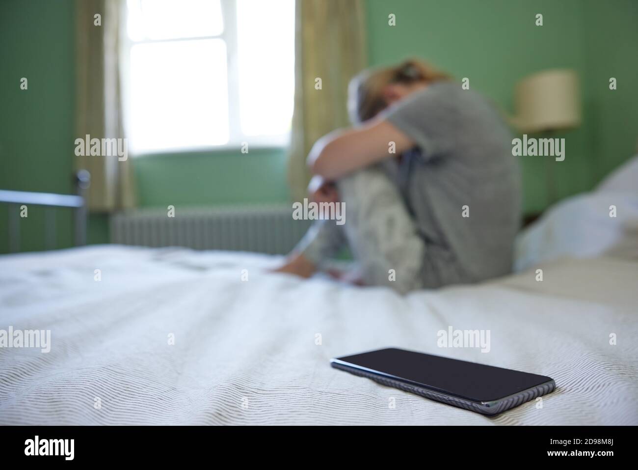 Jeune femme dans la chambre bouleversée par les médias sociaux de trolling et Cyber-intimidation sur téléphone mobile Banque D'Images