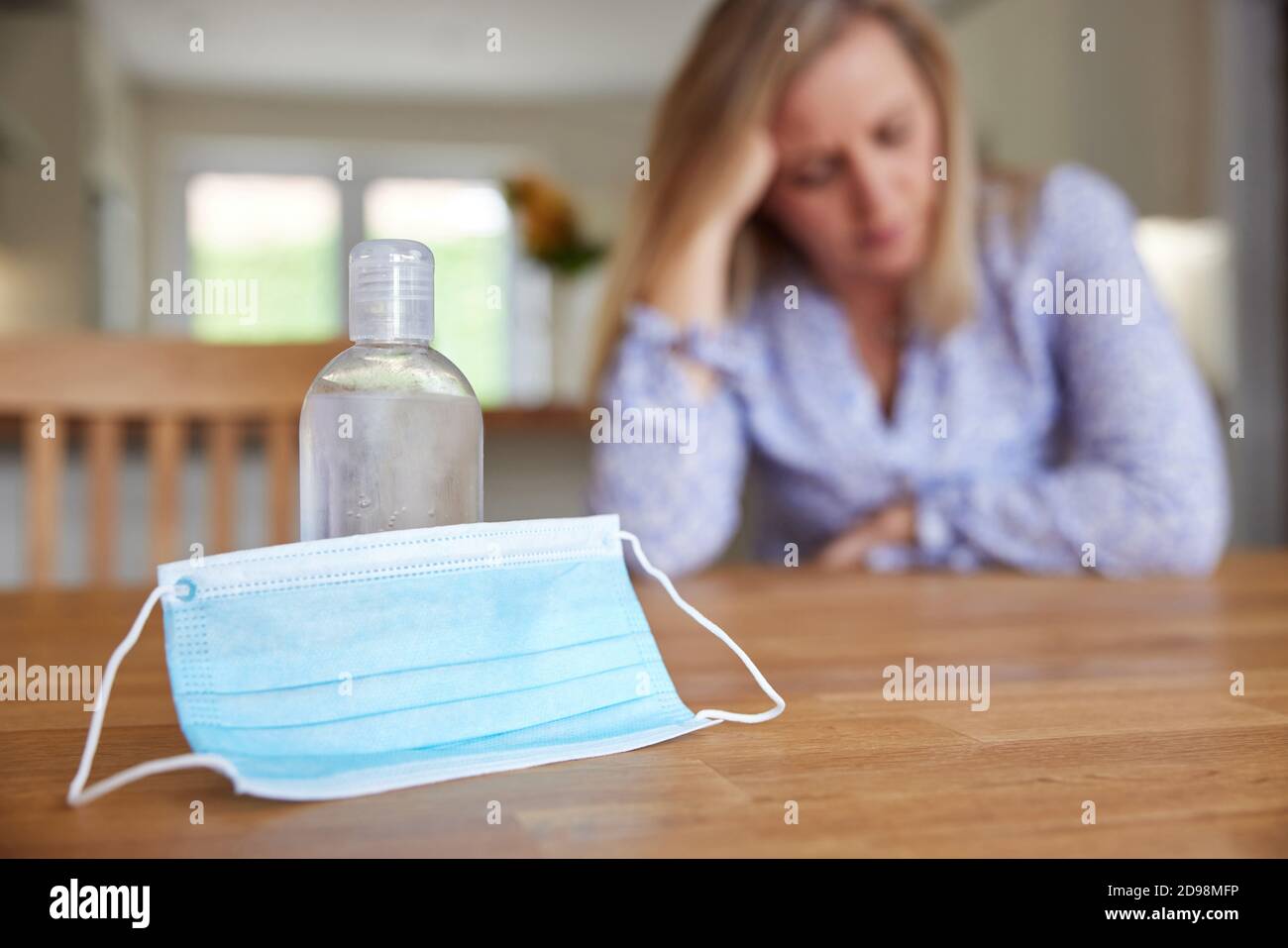 Femme dépressive assise à la maison pendant une pandémie avec masque facial Et bouteille d'assainisseur dans le premier plan Banque D'Images