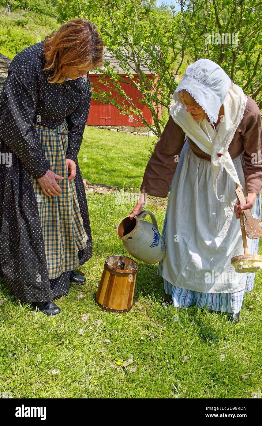 Deux femmes qui font du beurre, qui verse de la crème dans une urne ancienne, vêtues de jarretière coloniale, en plein air, interprètes bénévoles, Pennsylvanie, Hopewell Furnace Banque D'Images
