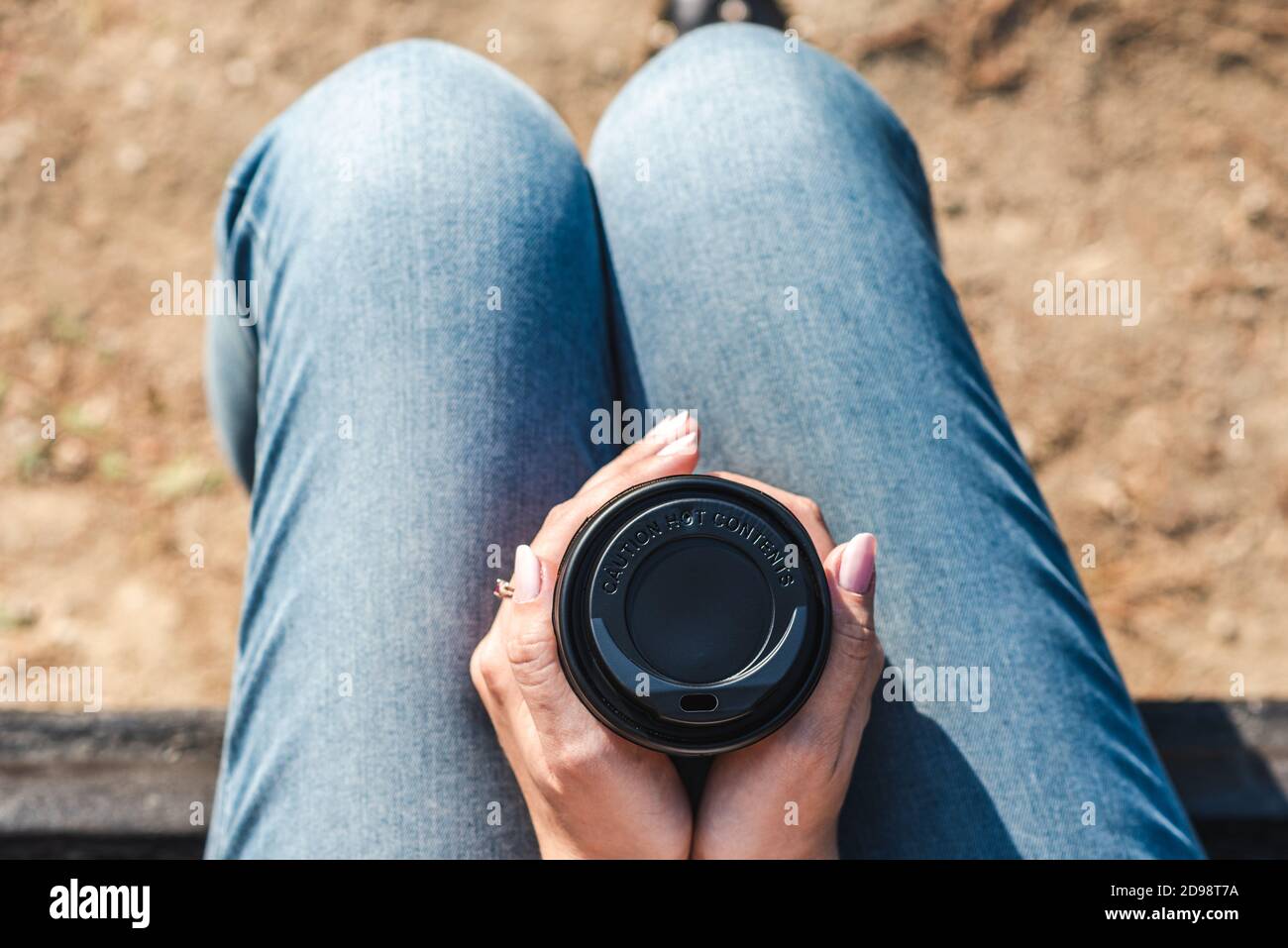 vue rapprochée du dessus d'une tasse à café à emporter avec un avertissement sur les matières chaudes et tenue par les mains d'une jeune femme caucasienne méconnaissable. Banque D'Images