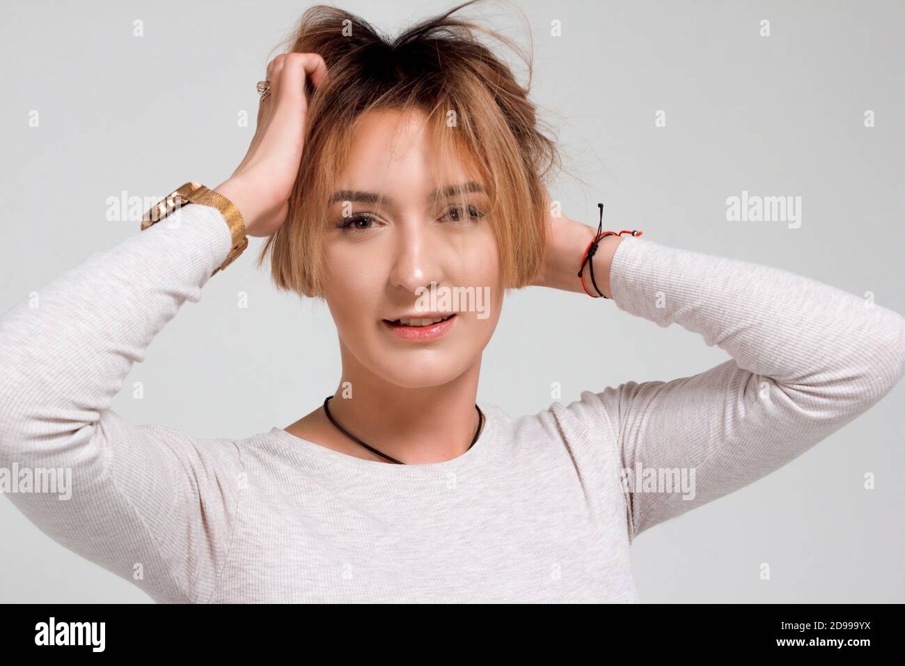 Portrait d'une jeune femme aux cheveux courts. Dans un chandail blanc et un pantalon vert. Sur fond blanc, il tient la tête dans ses mains Banque D'Images