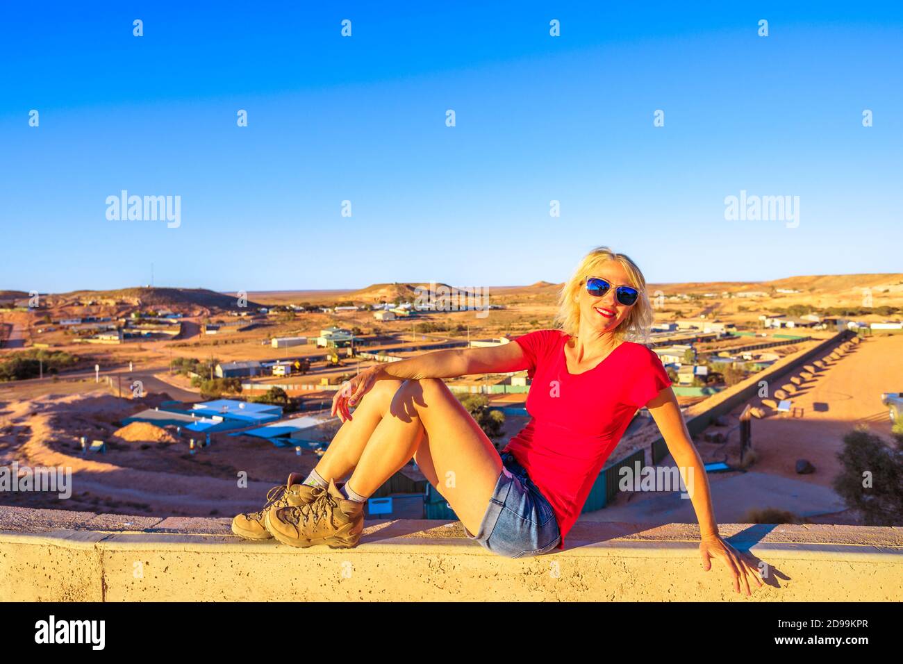 Femme touristique assise par une vue panoramique sur la ville souterraine de Coober Pedy au coucher du soleil et le désert environnant depuis le belvédère de la grotte. Outback sud-australien Banque D'Images