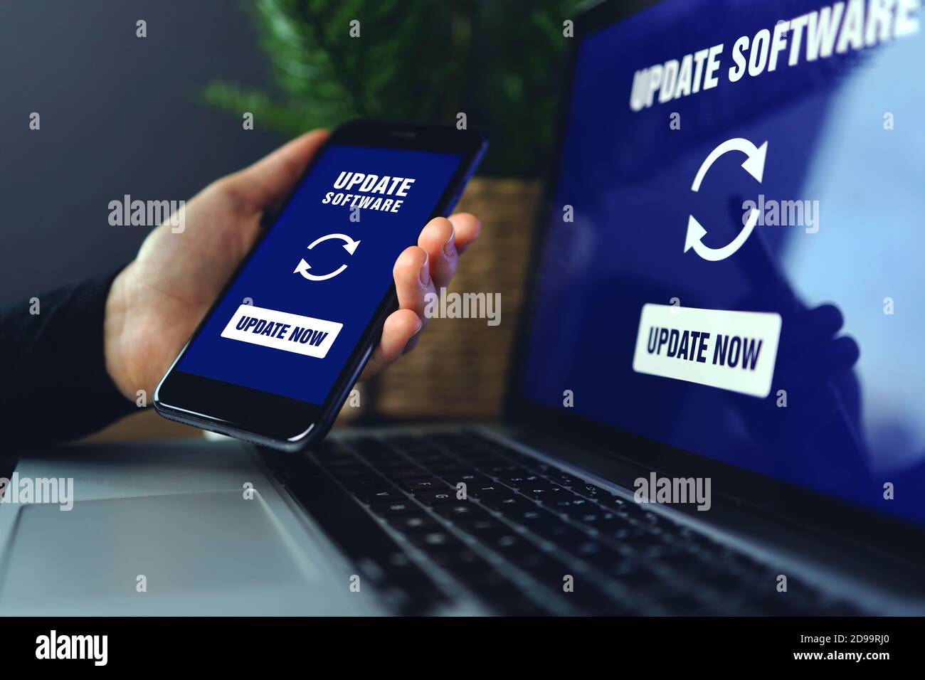 Main tenant le smartphone en train d'installer le processus de mise à jour avec le pourcentage de boîte de vitesses barre de progression et de chargement avec installation de la mise à jour sur l'écran de l'ordinateur portable arrière Banque D'Images