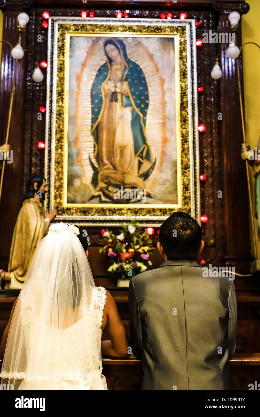 Juste marié à genoux suçant ensemble à la vierge de guadalupe dans l'église Banque D'Images