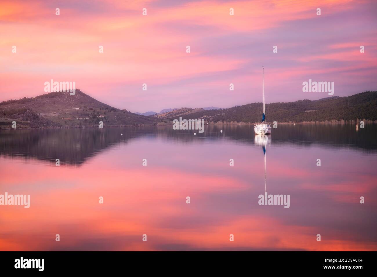 Pink Clouds et un voilier isolé se reflètent dans les eaux du lac carter, situé à Loveland, Colorado, lors d'une belle matinée printanière Banque D'Images