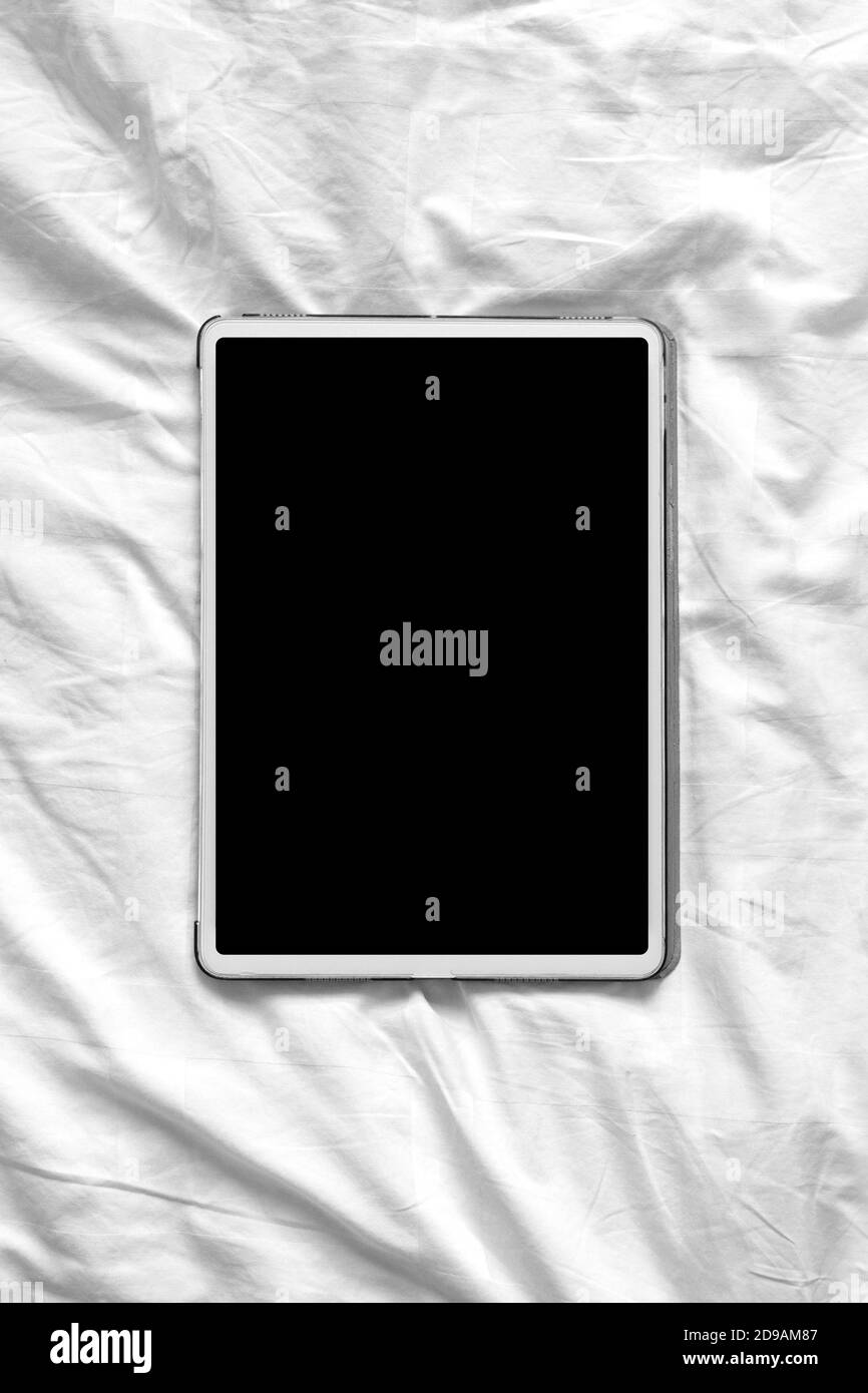 Vue de dessus maquette d'une tablette à écran vierge sur un lit blanc confortable à la maison. Orientation verticale de la photo Banque D'Images