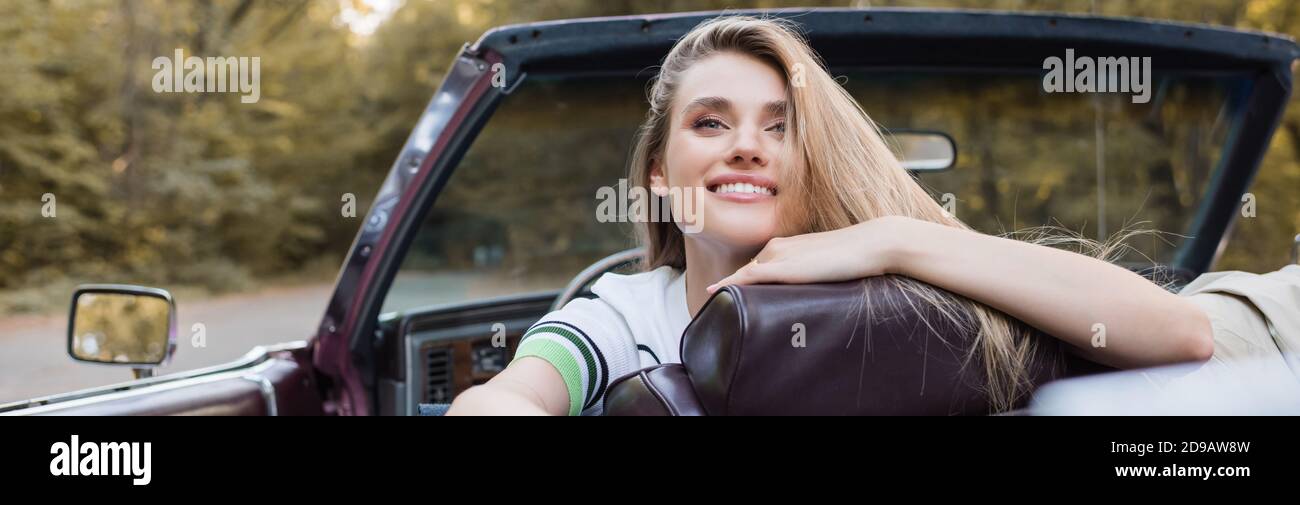 femme souriante regardant loin en étant assise dans une voiture convertible, bannière Banque D'Images