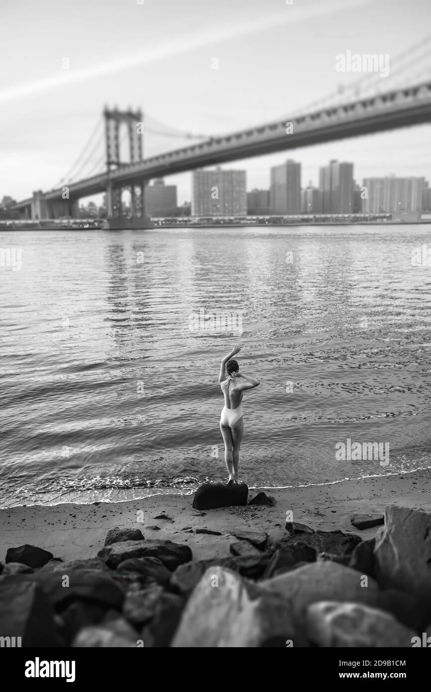 NEW YORK, États-Unis - 01 mai 2016 : image en noir et blanc d'une jeune femme en maillot de bain debout sur un rocher sur la rive de l'East River, sur le pont de Manhattan Banque D'Images