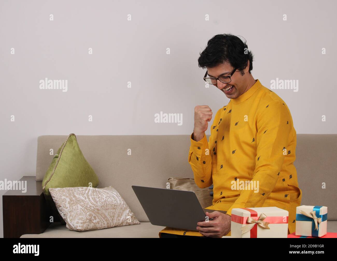 Jeune homme dans des lunettes et vêtements traditionnels assis à la maison à l'aide d'un ordinateur portable. Banque D'Images