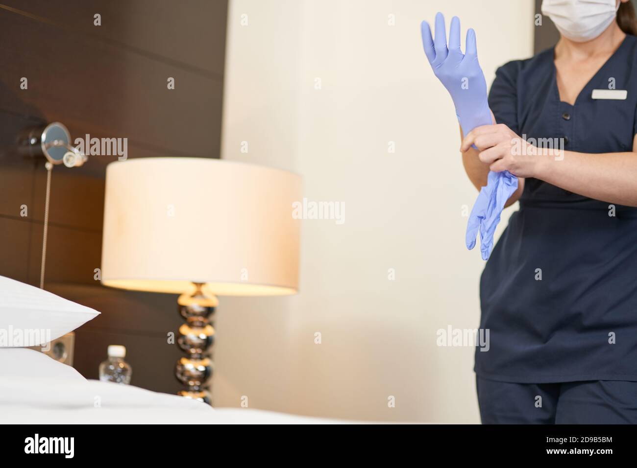 Photo rognée de la femme de ménage en uniforme en mettant des gants de protection avant le nettoyage. Concept de service d'hôtel Banque D'Images
